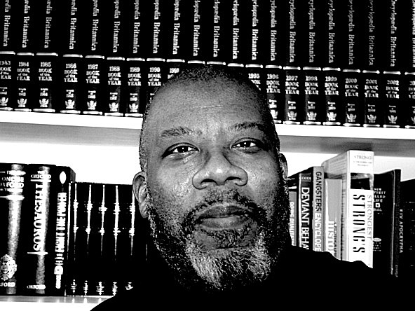 black and white image of Dr Kenny Monrose into front of a book shelf